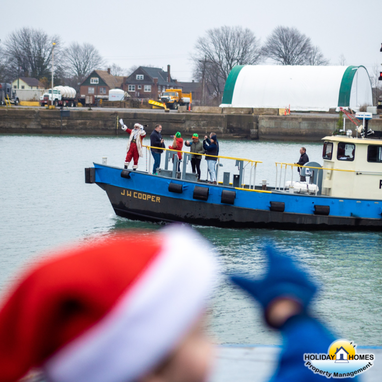 Santa Claus arrives by tugboat at the Port Colborne locks. He stands on the boat's deck, waving to the crowd gathered onshore. Credit: Holiday Homes Property Management.