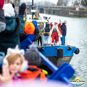 Santa Claus disembarks from the tugboat at the Port Colborne locks, warmly greeted by excited children. Smiling faces surround him as he steps onto the dock. Credit: Holiday Homes Property Management.